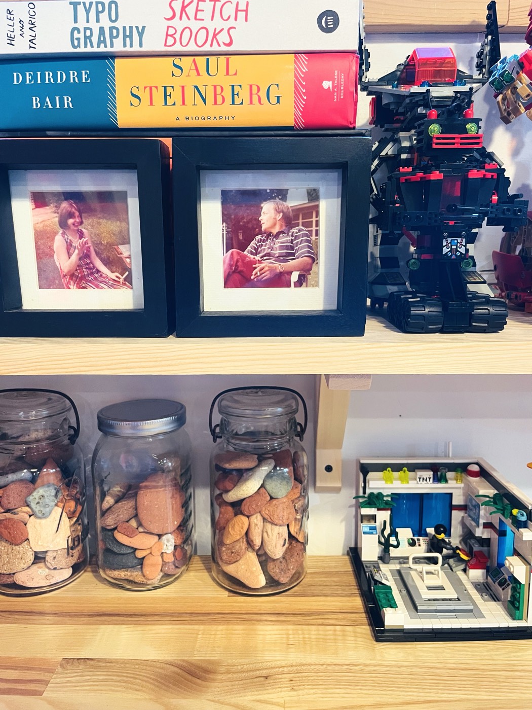 A shelf with design books, framed photos, and a LEGO robot sculpture